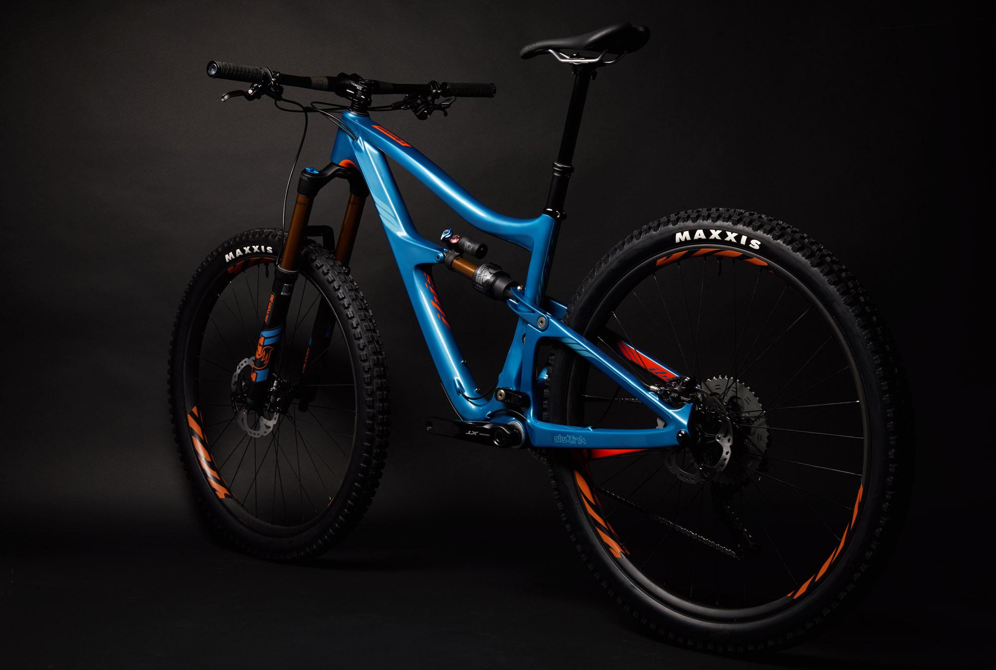 Ibis RipMo: A blue mountain bike with orange accents is positioned against a dark background. The bike features a full suspension design, thick tires with "MAXXIS" branding, and a modern frame. The image highlights the bike's sleek lines and robust components, showcasing it as a high-performance option for off-road cycling.