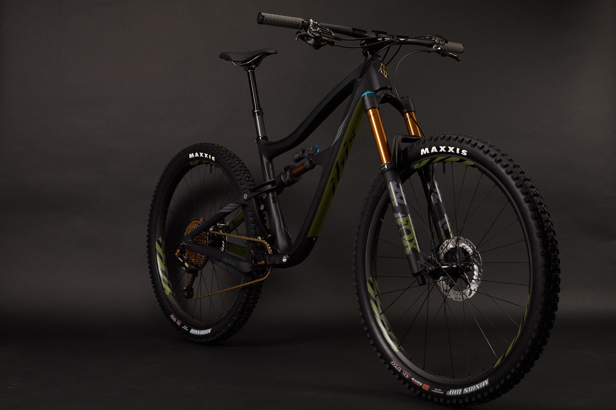 Ibis RipMo: A sleek mountain bike featuring a black frame with green accents, equipped with golden front suspension forks and Maxxis tires. The bike is positioned against a dark background, showcasing its design and components.