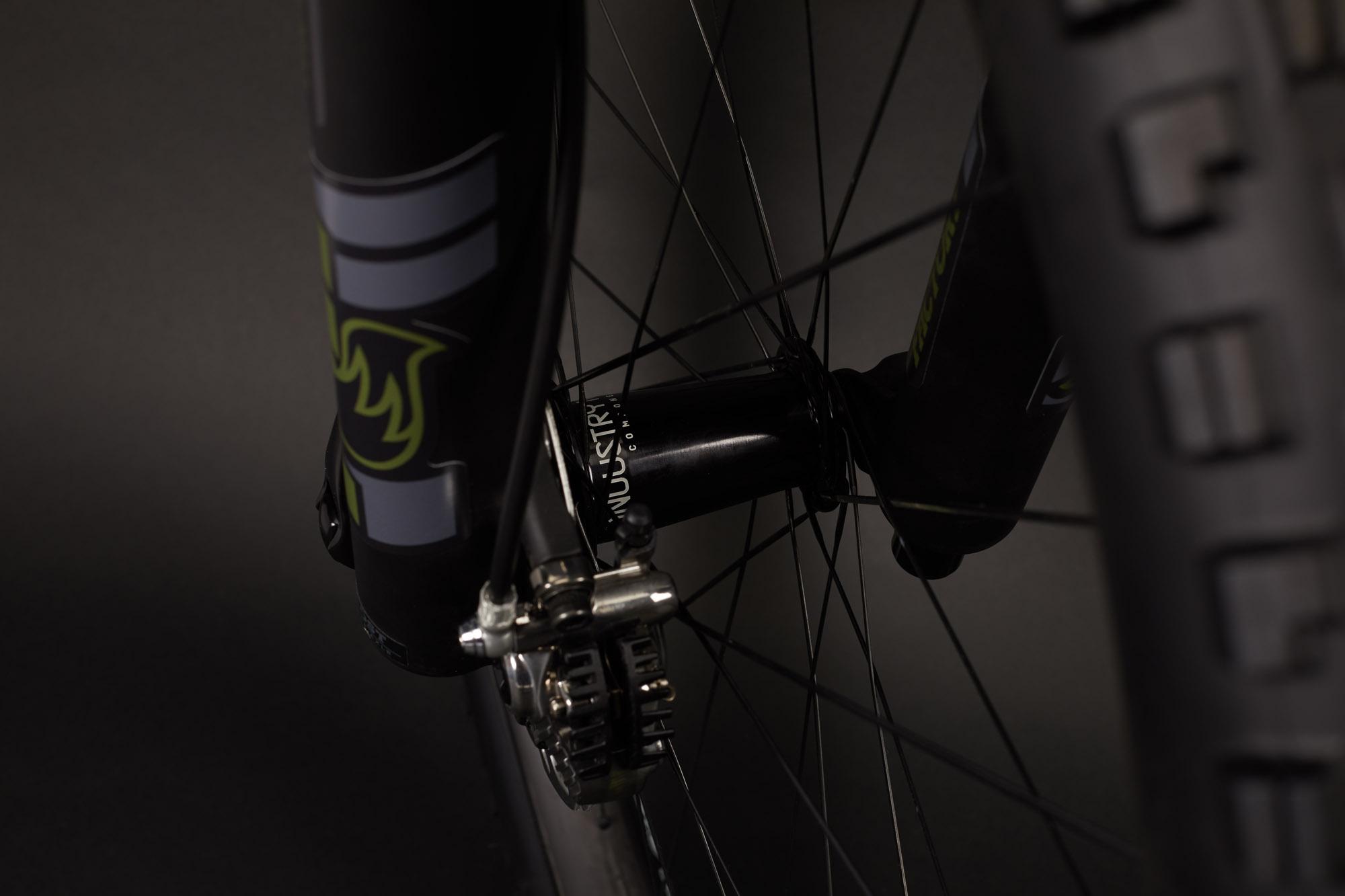 Ibis RipMo: Close-up view of a bicycle's front wheel, showcasing the hub, brake caliper, and spokes against a dark background. The wheel features sleek design elements and a visible logo on the hub.