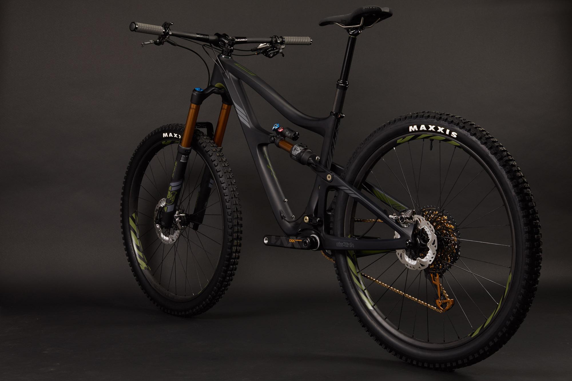 Ibis RipMo: A modern mountain bike featuring a sleek black frame with green accents, equipped with front suspension forks and knobby tires branded with "MAXXIS." The bike is positioned at an angle to showcase its design, including the drivetrain and seat, against a dark, neutral background.