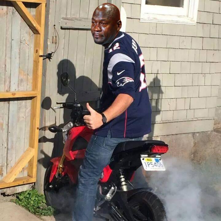 Salsa Timberjack: A person wearing a New England Patriots jersey gives a thumbs-up while sitting on a red motorcycle, surrounded by smoke. The background features a wooden structure.