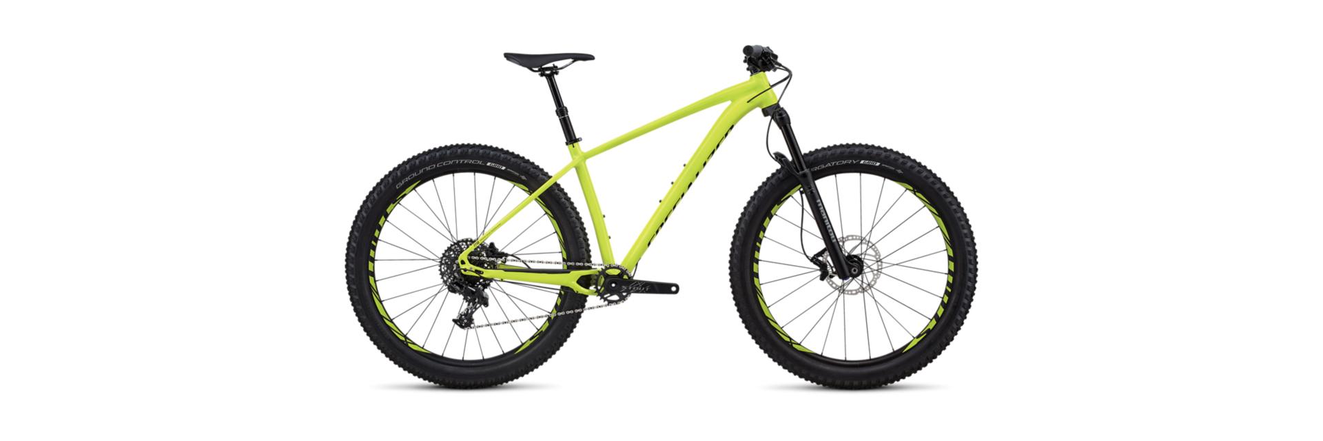 Specialized Fuse Comp 6Fattie: A bright yellow mountain bike with thick black tires, a streamlined frame, and disc brakes, positioned against a white background. The bike features a modern design, suitable for rugged terrain and outdoor adventures.