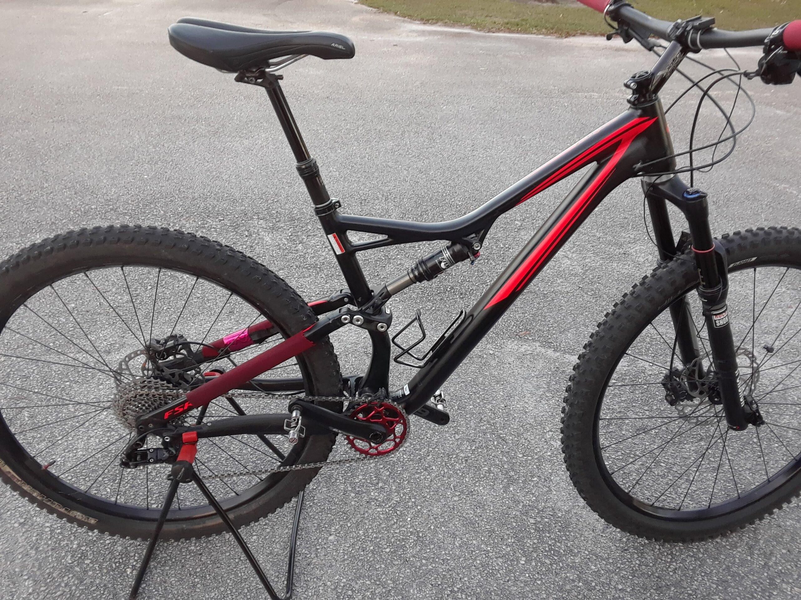 Specialized Stumpjumper FSR: Mountain bike with a black and red frame, featuring a dropper seat post, wide tires, and a rear suspension system, parked on a paved surface.