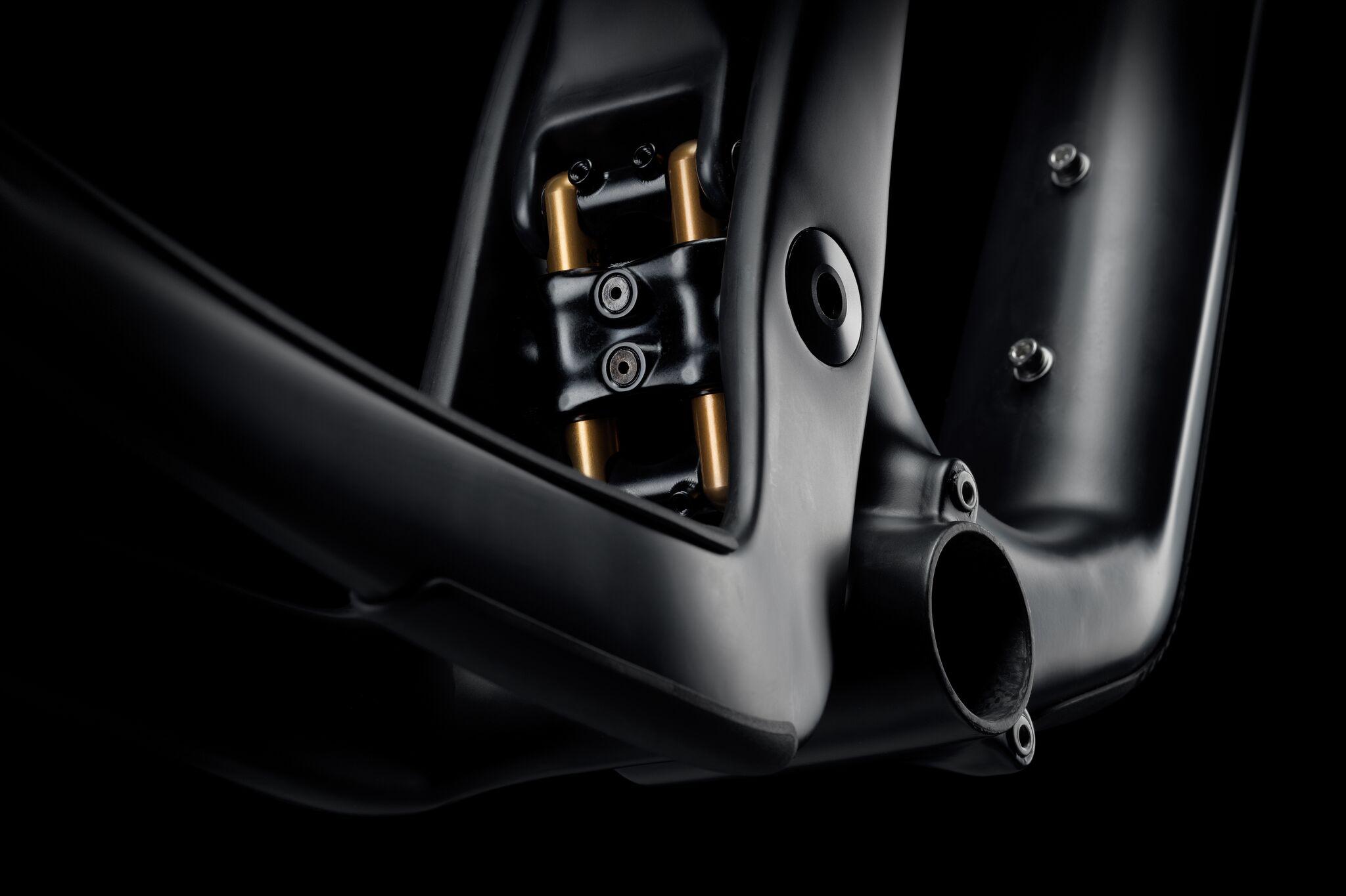 Yeti SB100: A close-up view of a black bicycle frame featuring a shock absorber with gold components, set against a dark background. The image highlights the frame’s sleek design and intricate detailing, including visible screws and openings.