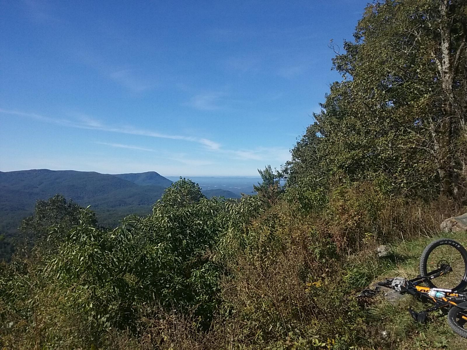 A scenic view of mountains under a clear blue sky, with lush greenery in the foreground and a bicycle lying on the ground, suggesting an outdoor adventure. Pinhoti Trail: P1 / Bear Creek Pinhoti mountain bike trail.