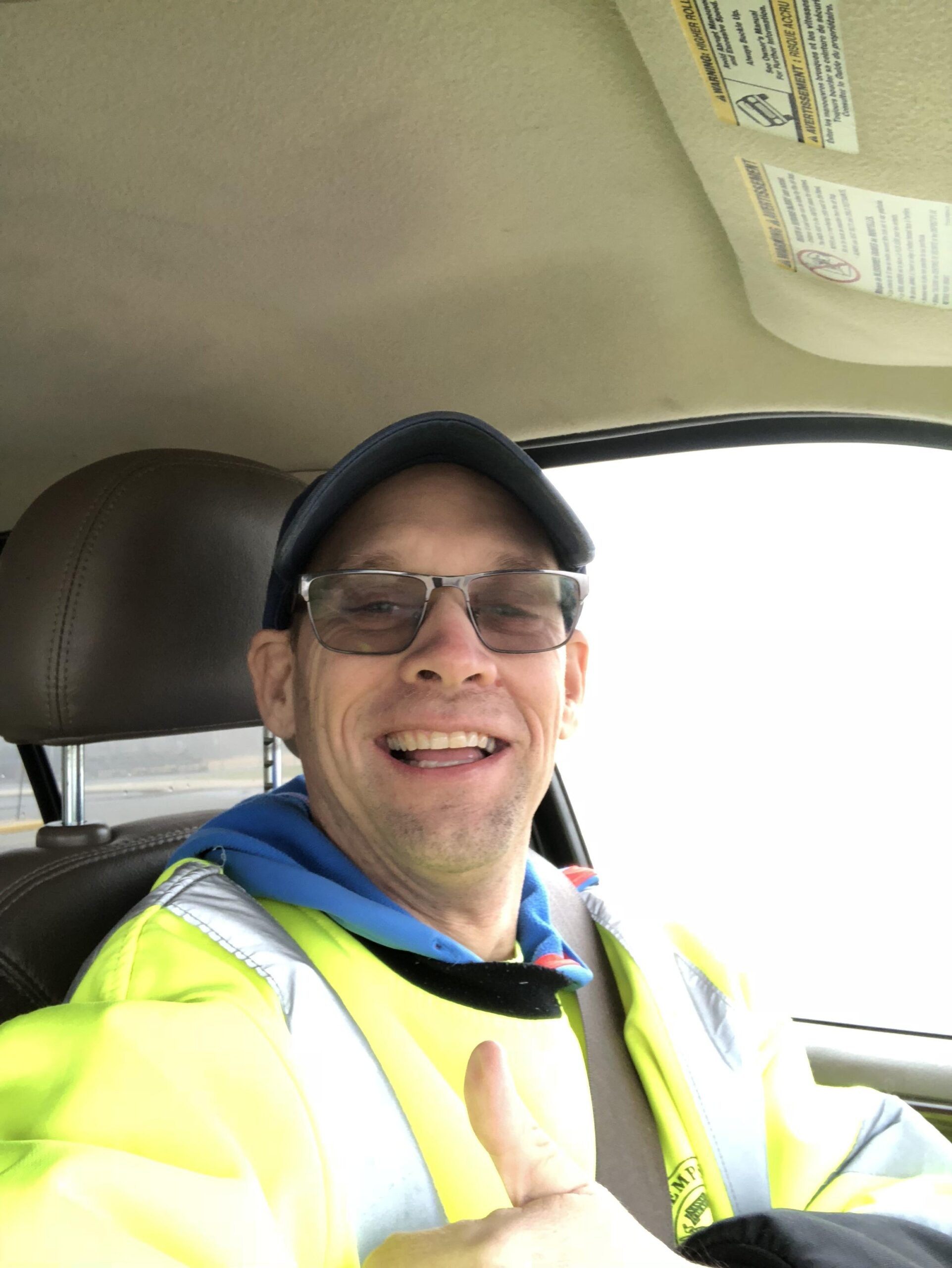 Giant Revel 29er: A man wearing glasses and a bright yellow safety jacket gives a thumbs up while seated in a car, smiling at the camera. The interior of the vehicle and the driver's seat are visible.