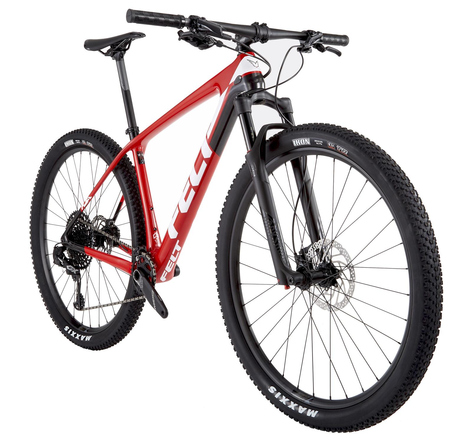 Felt Doctrine 3: A red mountain bike with a lightweight frame, featuring a black front fork and wide tires. The bike is equipped with a modern gear system and disc brakes, positioned at an angle to showcase its design and components.