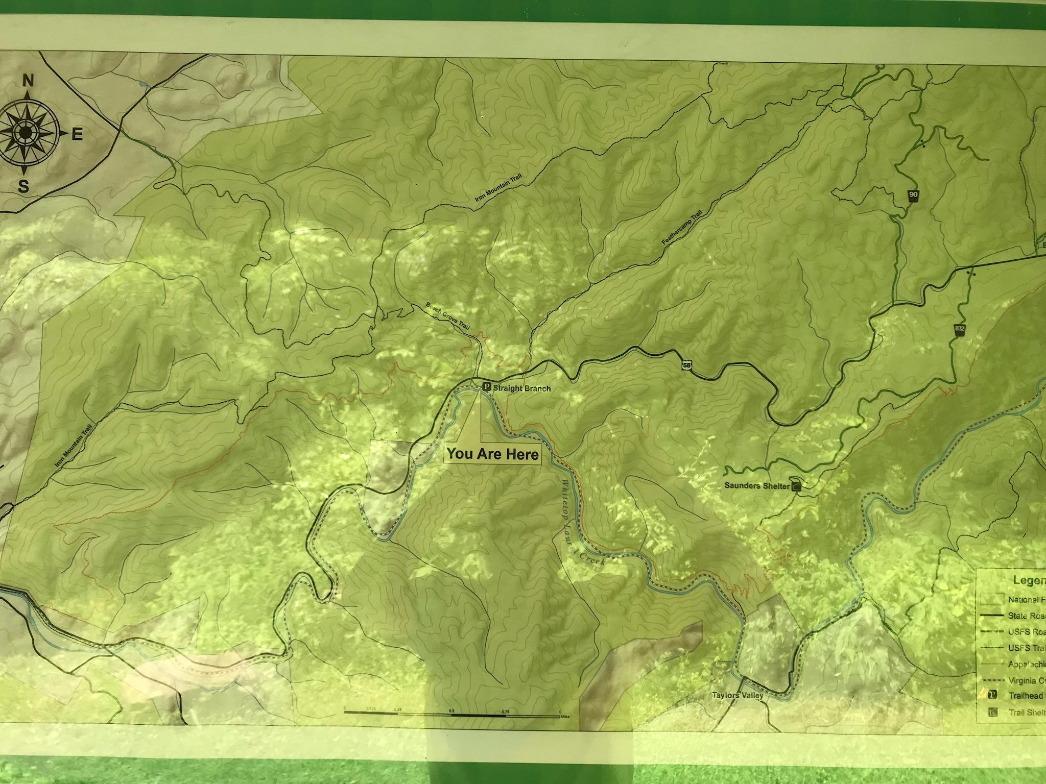 A topographic map displaying a mountainous area with various trails, rivers, and landmarks. The map includes a "You Are Here" marker, indicating the current location on the map. North is oriented at the top left, along with a compass rose. Other features include contour lines representing elevation changes and a legend for interpreting map symbols. Iron Mountain mountain bike trail.