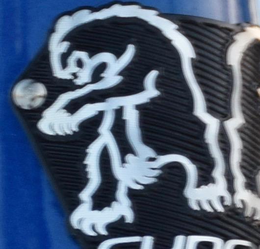 Chromag Rootdown: A close-up image of a black and white graphic featuring a stylized lion design, prominently displayed on a blue background. The lion appears in a dynamic pose, with its body arched and one paw raised. The graphic is positioned on a textured black surface with a metallic bolt visible in the corner.