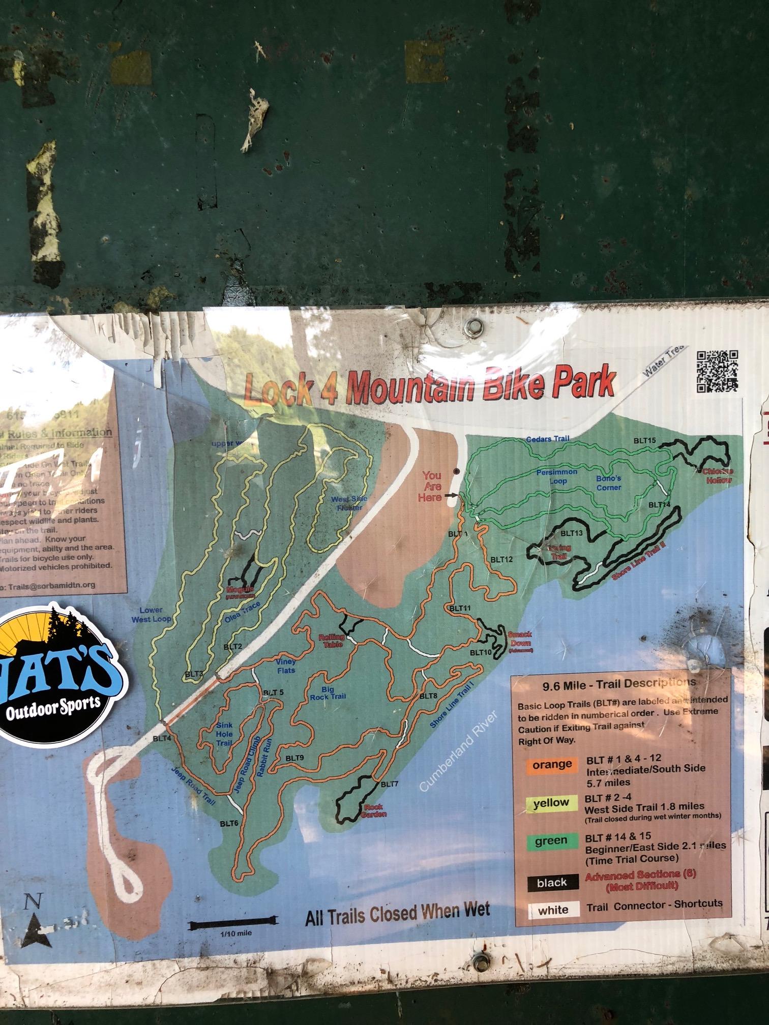 Map of Lock 4 Mountain Bike Park, displaying a trail overview with color-coded sections indicating different difficulty levels. The map includes labels for various trails, a scale, and a note that all trails are closed when wet. A logo for "Outdoor Sports" is visible on the side. Lock 4 mountain bike trail.