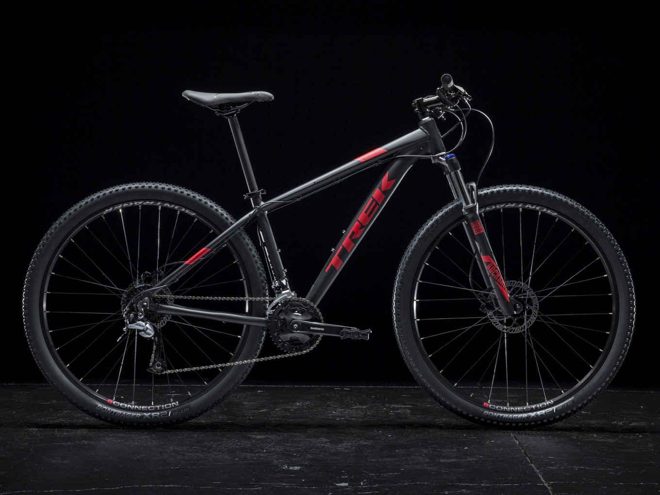 Trek Marlin 7: Mountain bike with a black frame and red accents, featuring rugged tires and a front suspension fork, set against a dark background.