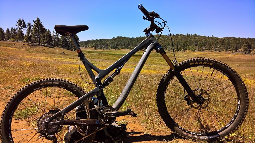 Intense Tracer 275c: A mountain bike positioned on a grassy field with trees in the background under a clear blue sky.