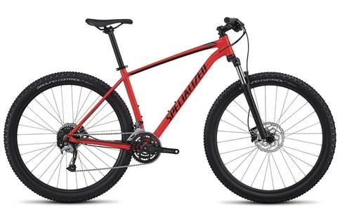 Specialized Rockhopper: A red mountain bike with a sleek frame, wide tires, and front suspension, featuring the brand name "Specialized" prominently displayed. The bike is shown from the side, highlighting its design and components suitable for off-road cycling.