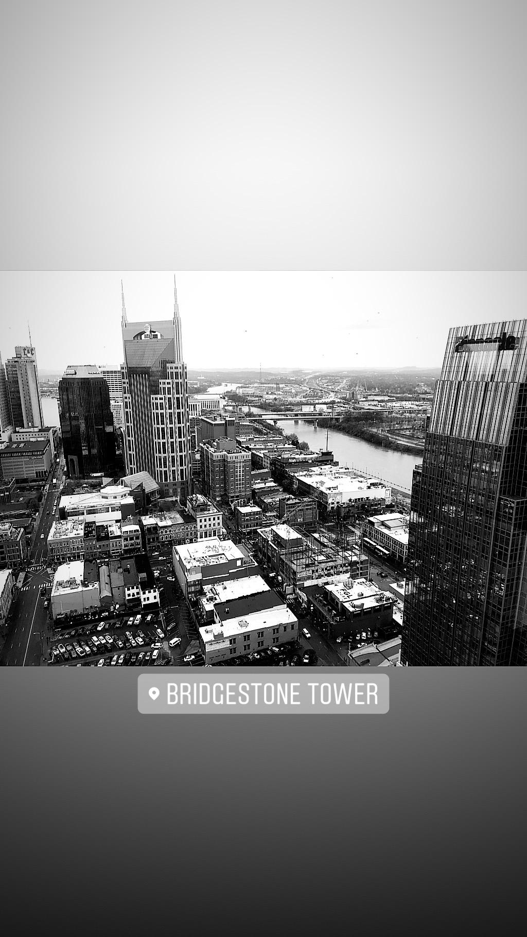 A black and white aerial view of a city skyline, featuring several high-rise buildings with a river flowing in the background. The image includes the Bridgestone Tower prominently displayed, along with various rooftops and streets below. Lock 4 mountain bike trail.