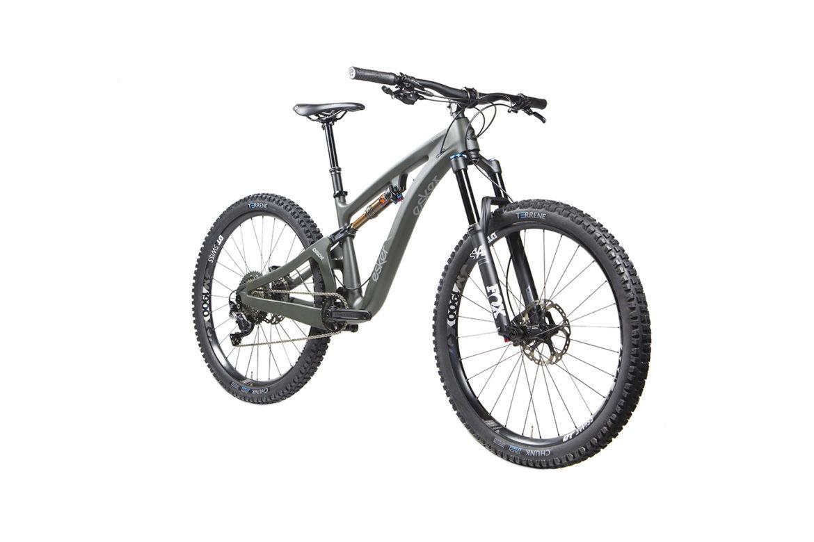 Esker Elkat: A modern mountain bike with a sleek design, featuring a dark green frame, front suspension fork, and knobby tires. The bike is shown from a side angle, highlighting its sturdy build and high-performance components, ideal for off-road cycling.