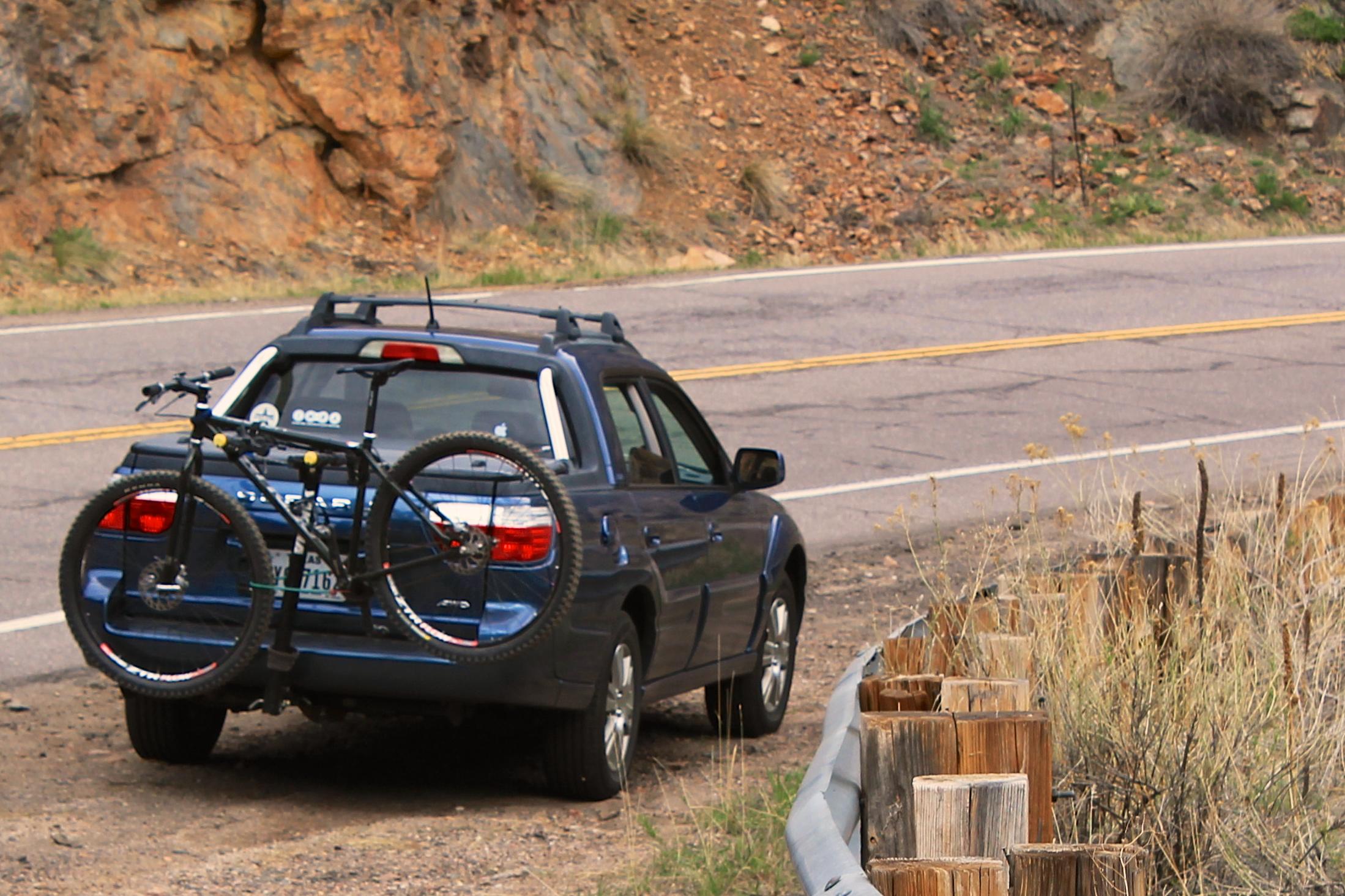 Redline Monocog 29er: A blue SUV parked near a winding road, with a mountain bike secured on a rack mounted to the back. The background features rocky terrain and sparse vegetation.