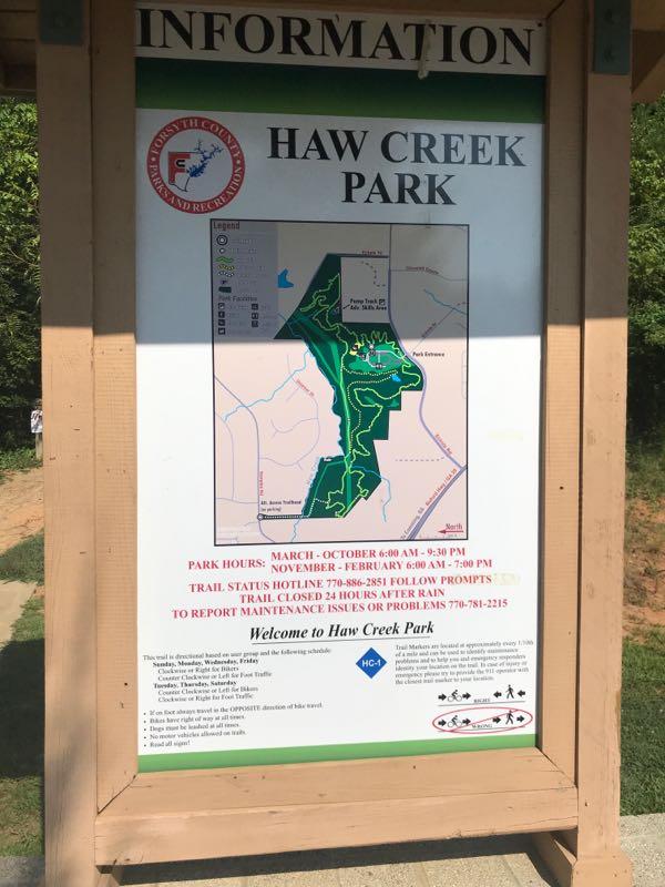 Signboard displaying information about Haw Creek Park, including park hours, a trail map, and contact information for maintenance issues. The map highlights various trails and points of interest within the park. Haw Creek Park mountain bike trail.