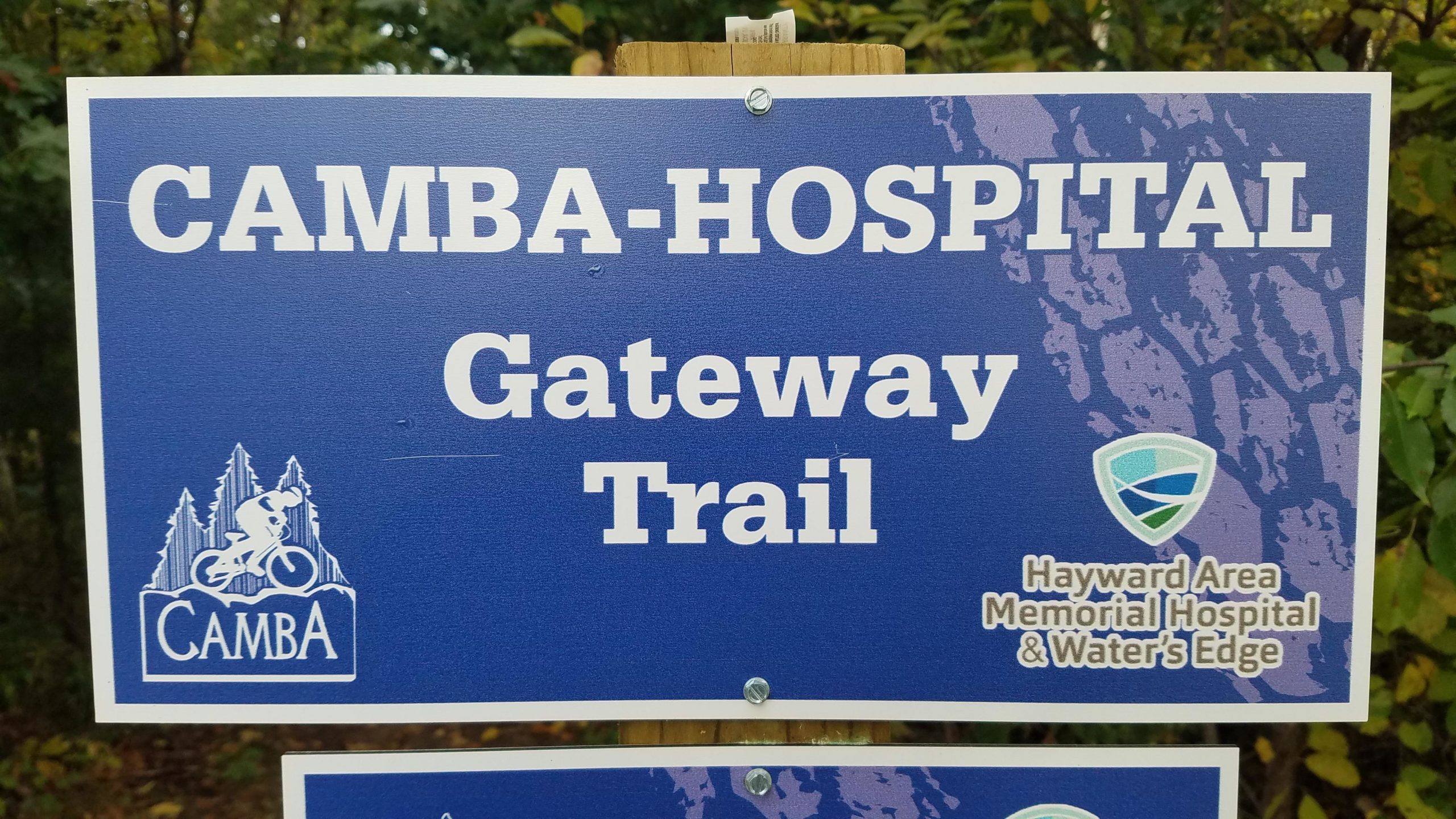 Sign for the CAMBA-Hospital Gateway Trail featuring the CAMBA logo with a cyclist and the logo for Hayward Area Memorial Hospital & Water