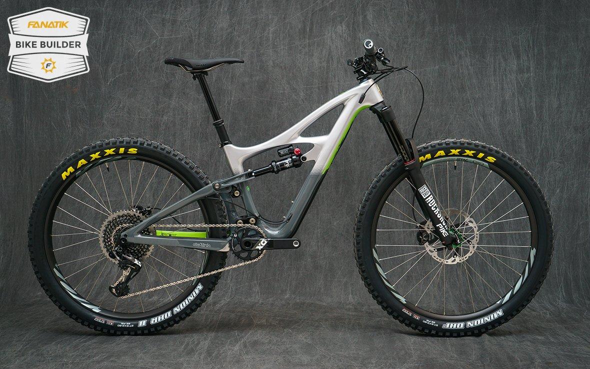 Ibis Mojo HD4: A modern mountain bike with a gray and green frame, featuring thick Maxxis tires, a front suspension fork, and a sleek design. The bike is oriented to showcase its side profile against a dark textured background.