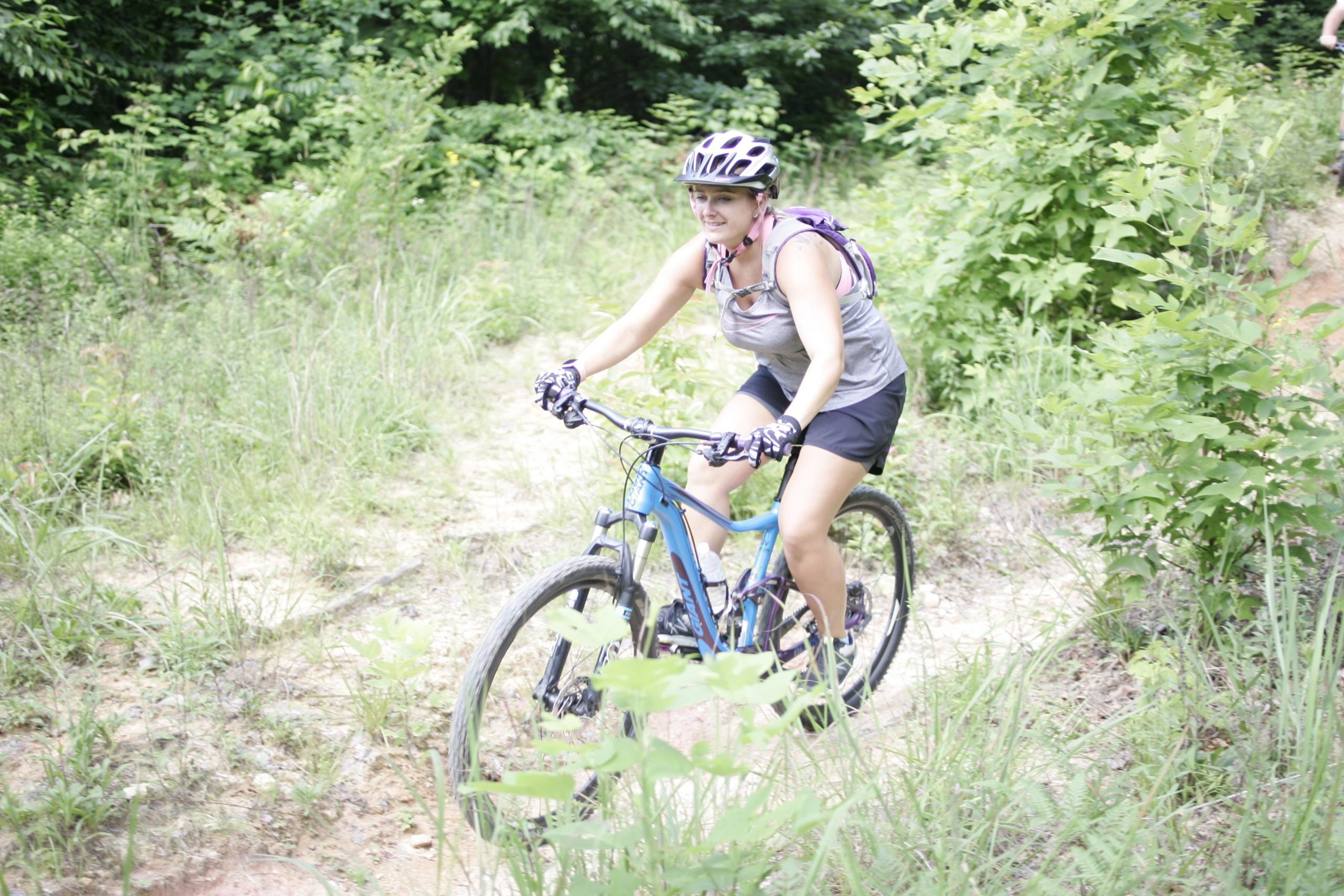 A person riding a mountain bike on a dirt trail surrounded by lush green foliage, wearing a helmet and cycling gear. Table Rock mountain bike trail.