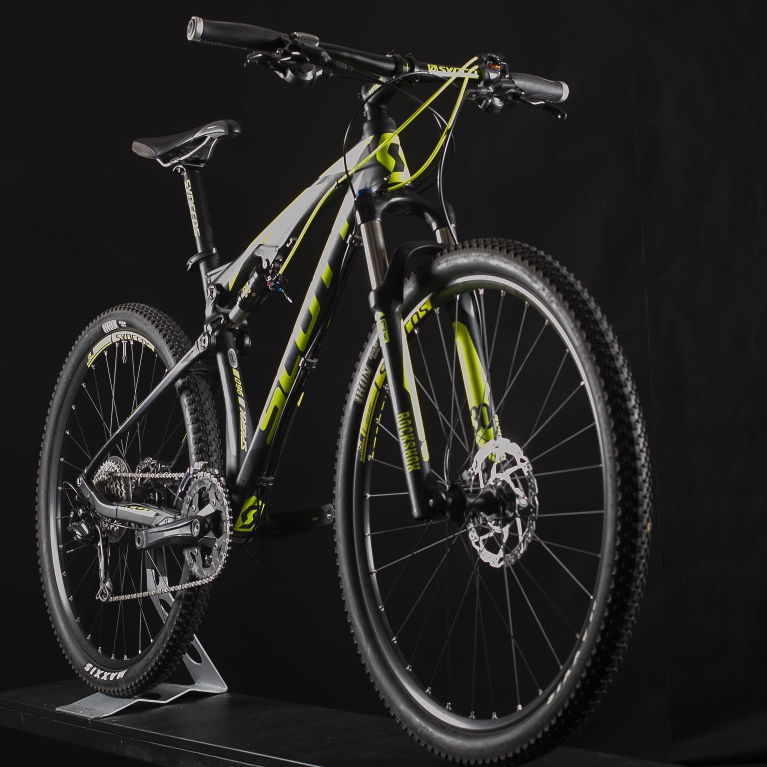 Scott Spark 960: A detailed image of a mountain bike with a black and green color scheme, featuring large, textured tires and a robust frame. The bike is positioned on a stand against a black backdrop, showcasing its components including the suspension system, gears, and handlebars.