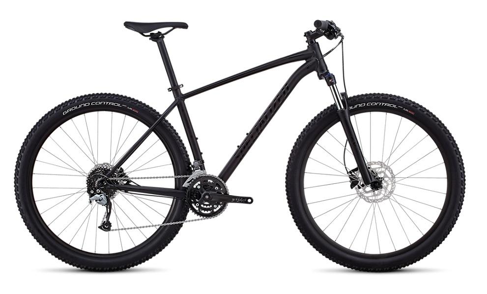 Specialized Rockhopper Comp 29: A black mountain bike with wide tires, front suspension, and a sleek frame design, displaying components such as disc brakes and a gear shifter. The bike is positioned on a plain background, emphasizing its features and modern aesthetic.