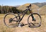 Yeti SB4.5c: A mountain bike is parked on a dirt trail with a scenic backdrop of rolling hills and trees. The sky is clear, and the landscape suggests a recreational outdoor setting.