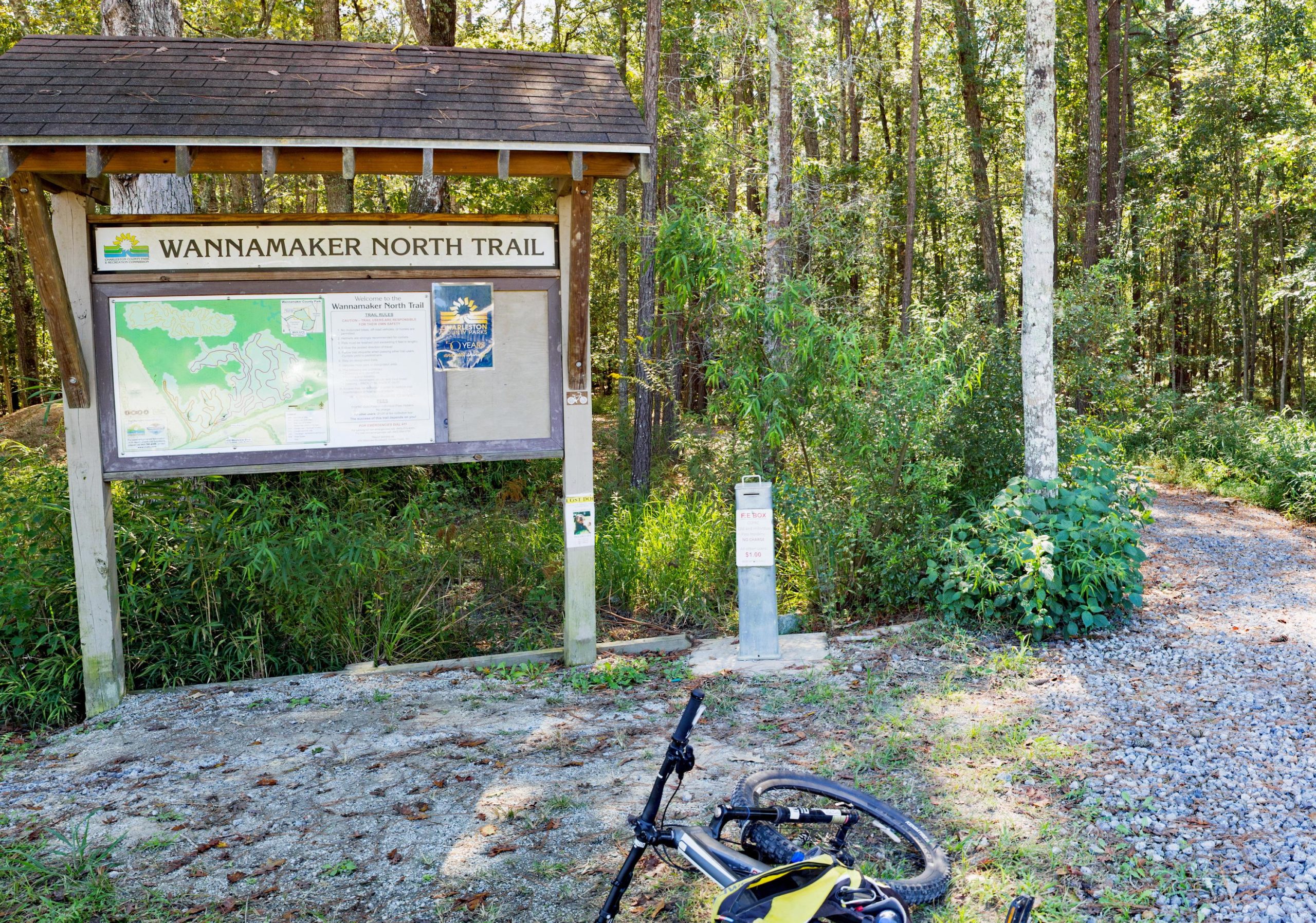 Sign for the Wannamaker North Trail, featuring a trail map, rules, and information, surrounded by greenery, with a bike resting on the ground nearby. Wannamaker Park mountain bike trail.
