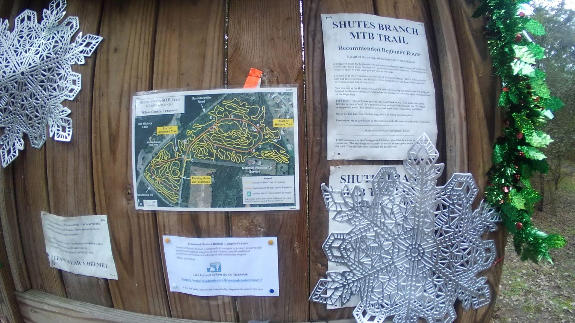 Signage at Shutes Branch MTB Trail featuring a map of the trail system, recommended beginner routes, and safety information, decorated with festive snowflake cutouts. Shutes Branch mountain bike trail.