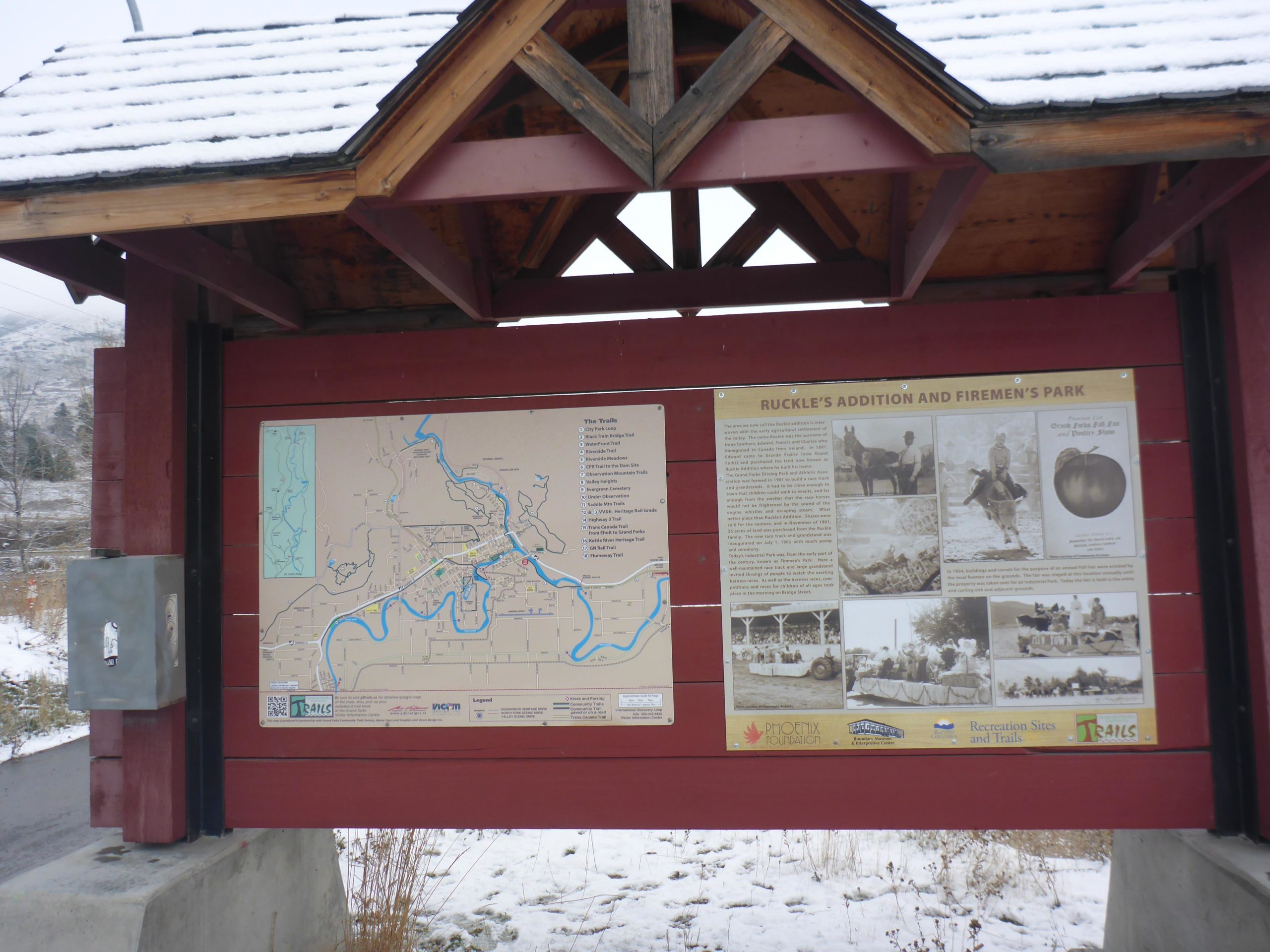 Map and informational display at Ruckle's Addition and Firemen's Park, featuring a trail map and historical photographs, under a roof with a snow-covered top. Trans Canada Trail - Grand Forks to Christine Lake mountain bike trail.