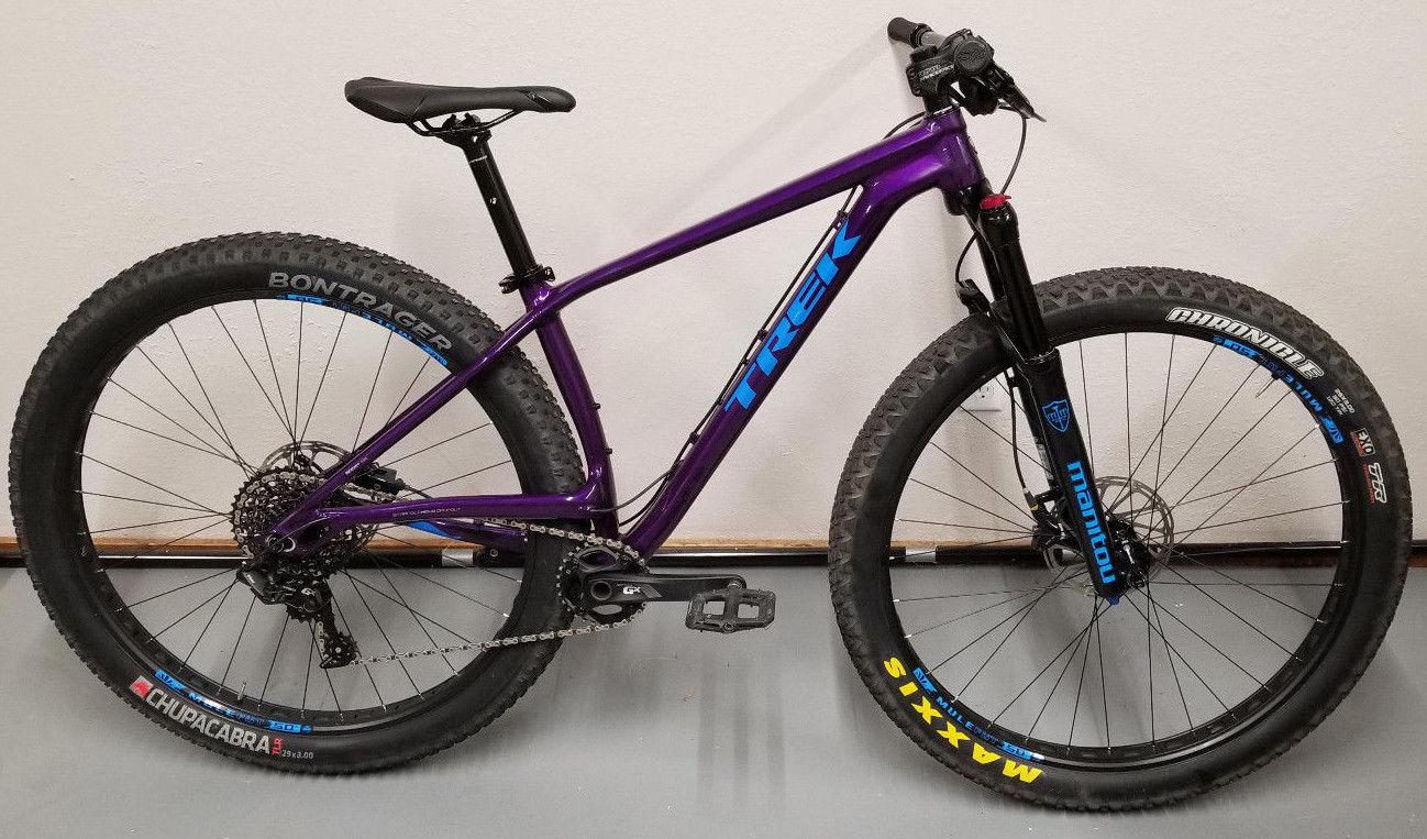 Trek Stache 7: A purple mountain bike with thick tires, featuring a lightweight frame, disc brakes, and a suspension fork. The bike is displayed against a plain background and has components branded with the names Bontrager and Maxxis.