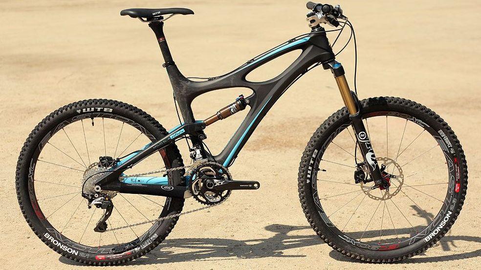 Ibis Mojo SL-R: A black and blue mountain bike, featuring wide, knobby tires, an adjustable seat, and a sturdy frame, displayed on a sandy background.