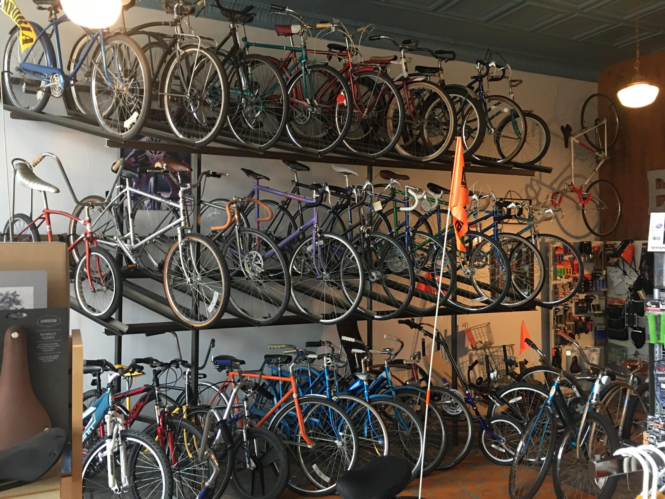 A bicycle shop interior displaying a variety of bicycles arranged on multiple shelves. The bikes come in different colors and styles, showcasing an assortment of models. In the foreground, there are bicycle accessories and parts visible on display. The shop has a warm, inviting atmosphere with soft lighting.