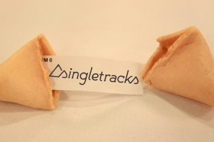 A broken fortune cookie with a paper slip inside that reads "singletracks," placed on a light-colored surface.