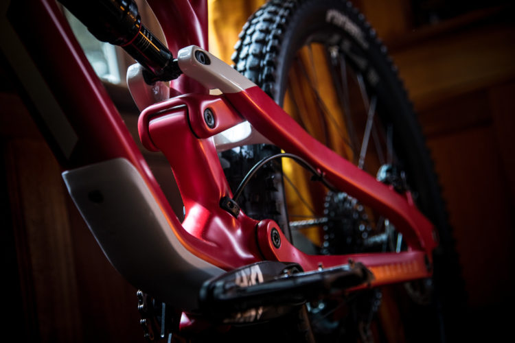 Close-up view of a red bicycle frame showcasing the suspension linkage and components in a well-lit indoor setting. The focus is on the intricate details of the frame design, highlighting both the craftsmanship and the mechanical parts.