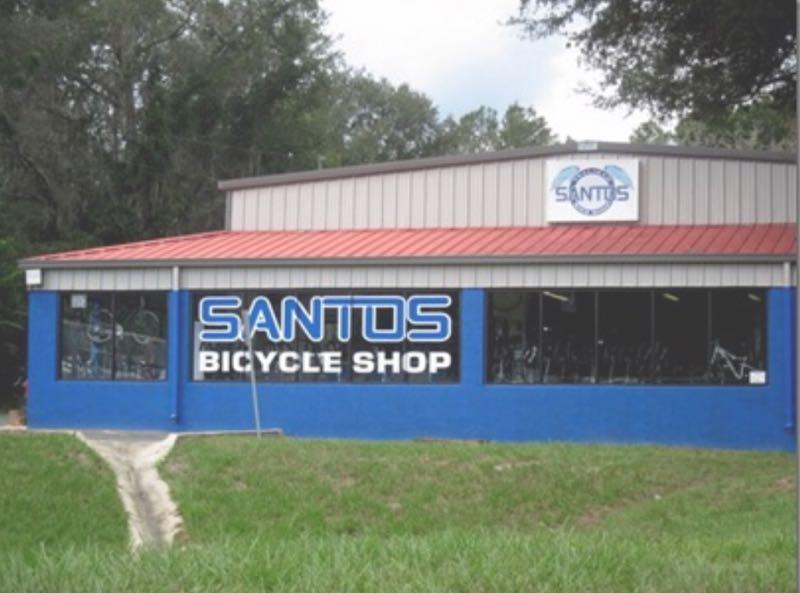 Alt text: Exterior view of Santos Bicycle Shop, featuring a blue building with large windows displaying bicycles. The shop