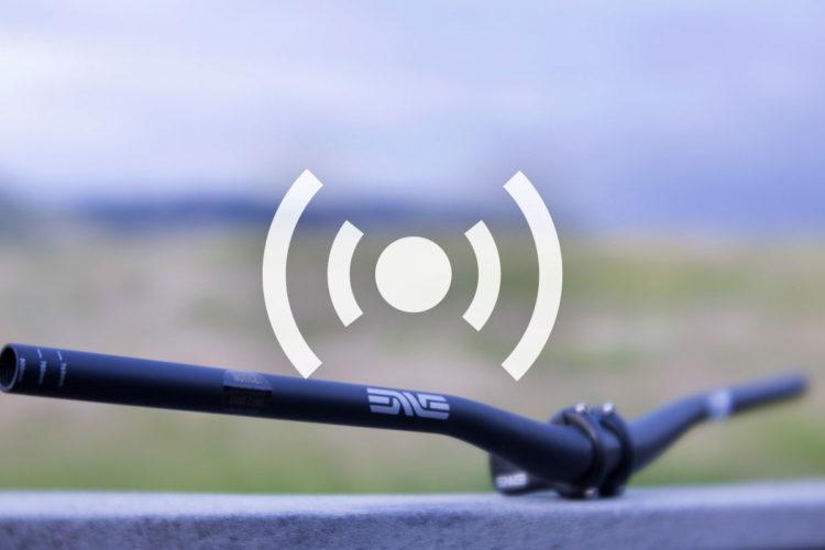 A black bicycle handlebar positioned in the foreground with a blurred natural landscape in the background. A circular signal icon is superimposed over the image.