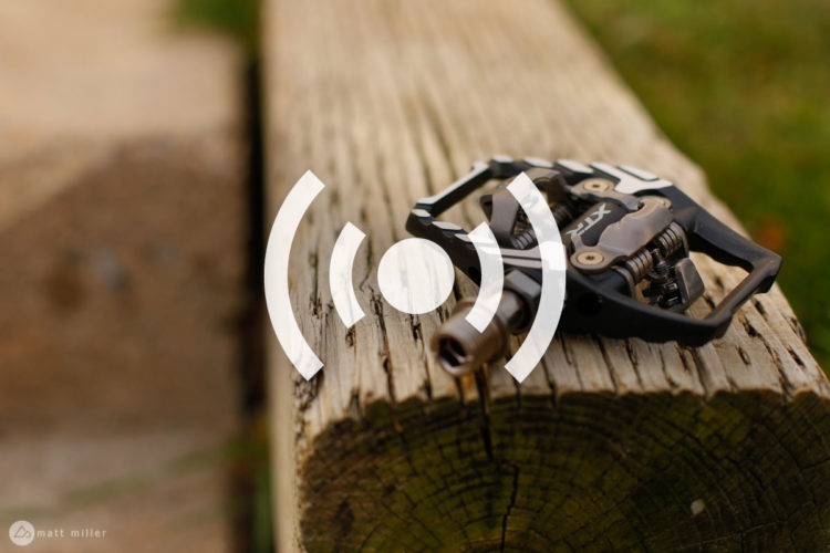 Close-up of a black bicycle pedal resting on a wooden surface, with a blurred natural background.