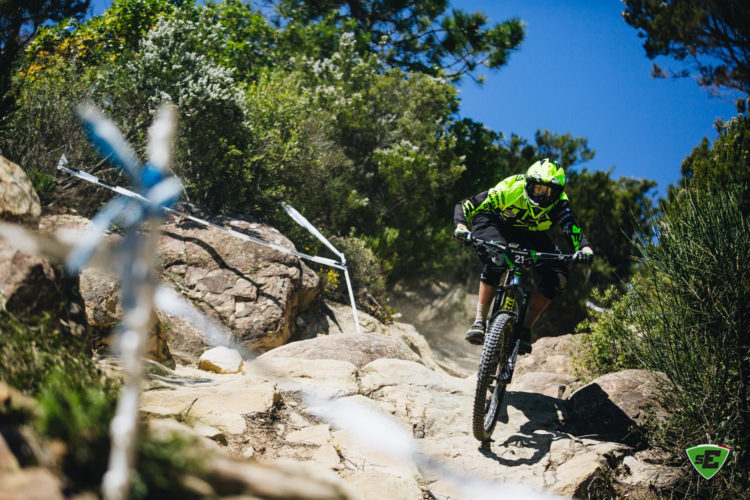 A mountain biker in bright green gear descends a rocky trail surrounded by greenery, showcasing the excitement and skill of downhill biking.