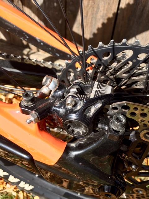 Rocky Mountain Instinct C70: Close-up view of a bicycle's rear brake system, showcasing the black brake caliper, disc rotor, and chainstay. The bicycle frame features an orange and black color scheme, with visible bolts and components highlighting the intricate mechanics of the braking system.