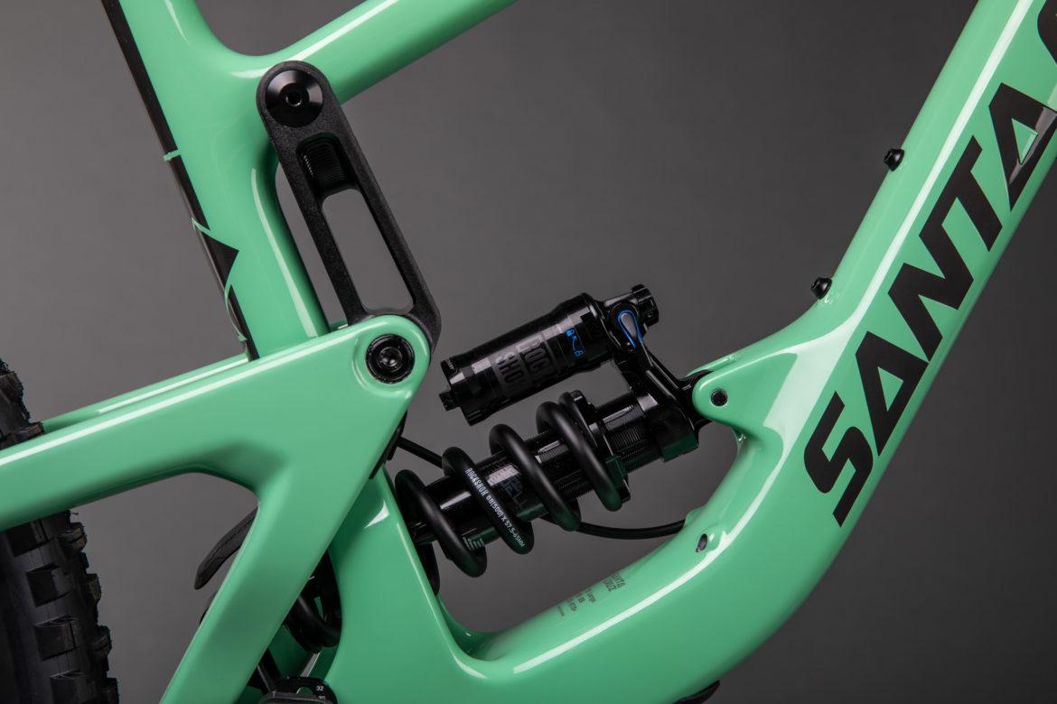Santa Cruz Megatower: Close-up view of a mint green mountain bike frame featuring a black shock absorber and coil spring. The background is a neutral gray, highlighting the bike's design and components.