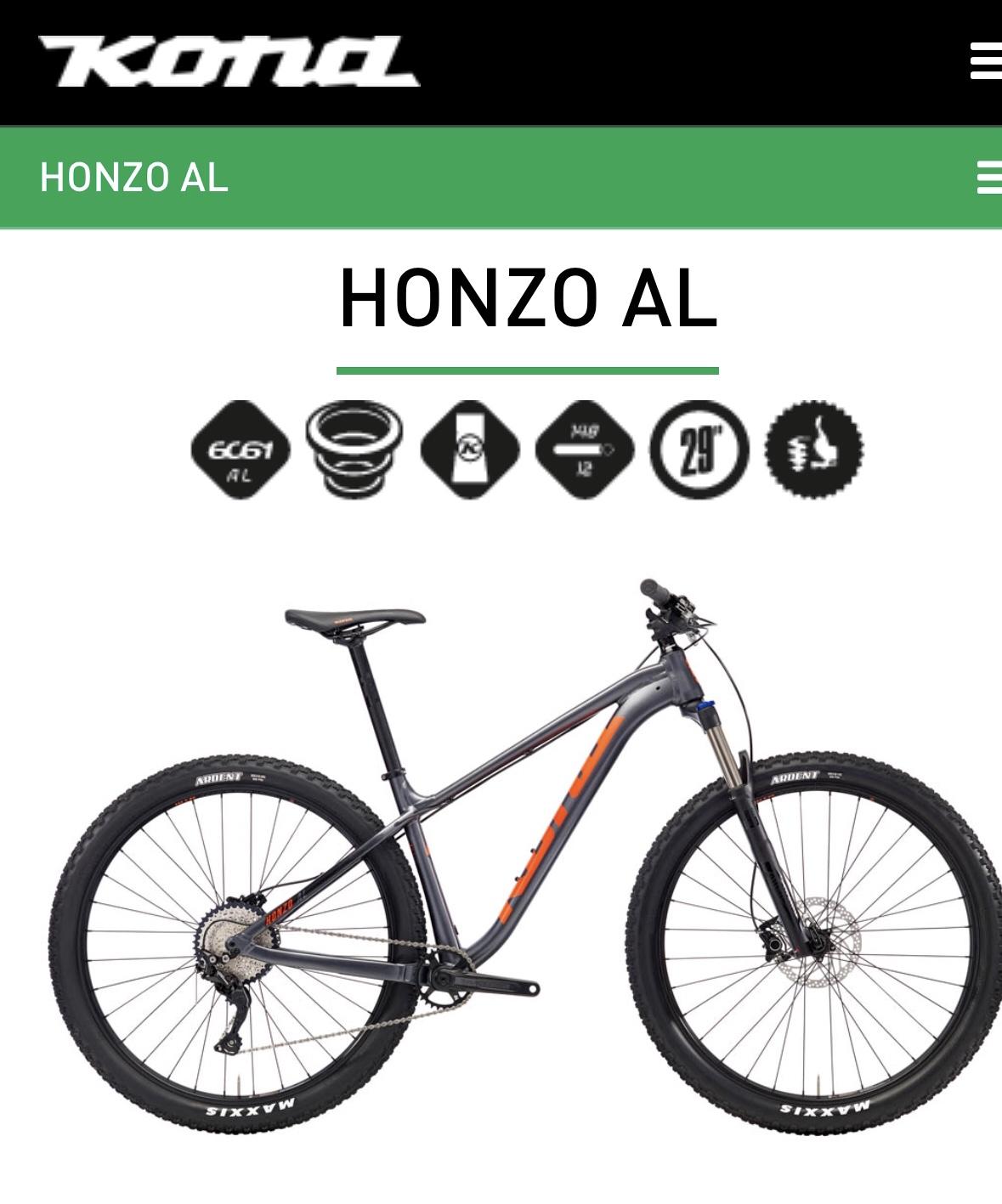 Kona Honzo: Alt text: A Kona Honzo AL mountain bike displayed on a white background, featuring a sleek gray frame with orange accents, and equipped with 29-inch wheels and rugged tires. The image includes specifications and branding at the top.