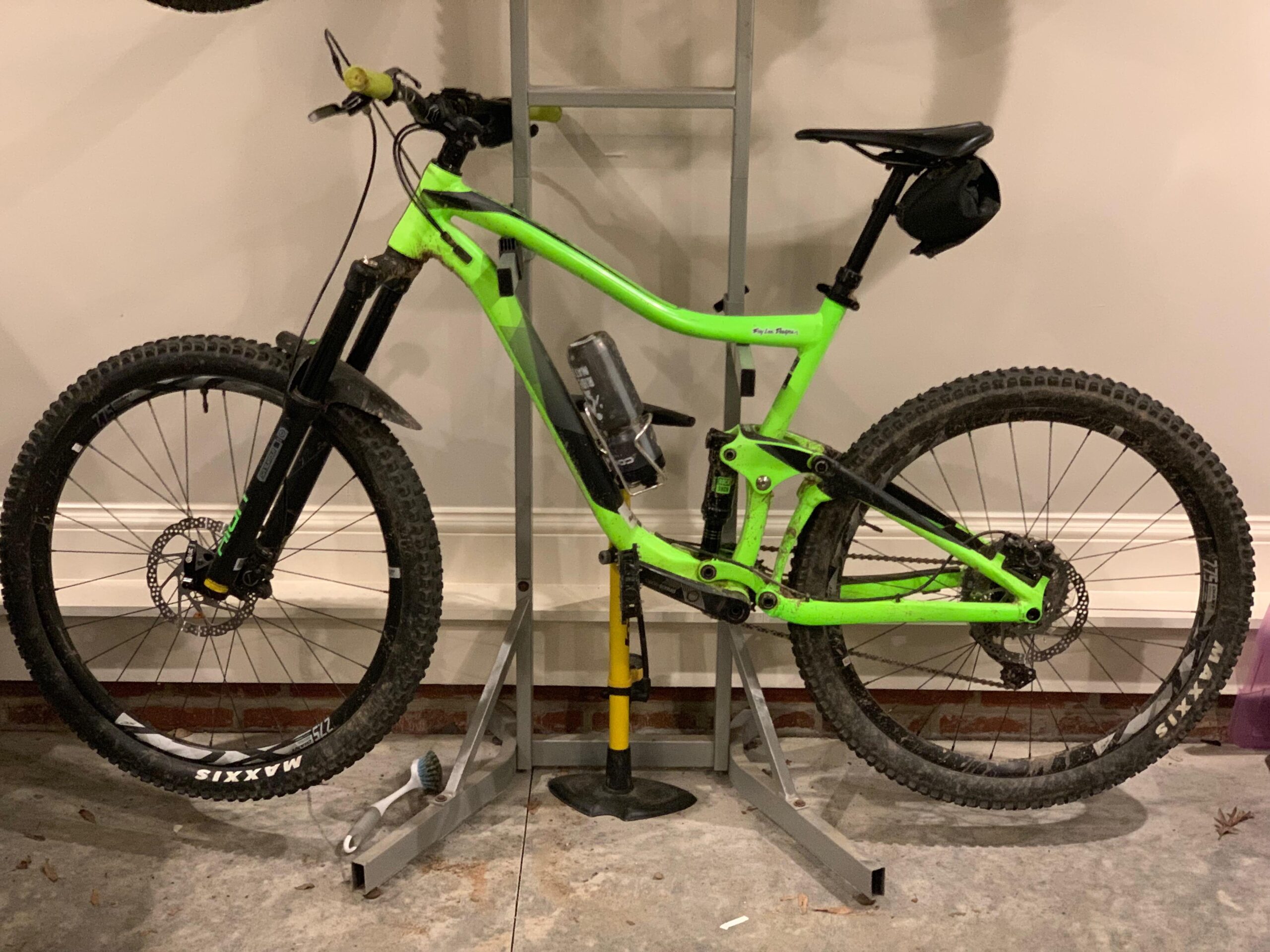 Giant Giant Trance 27.5 2: A bright green mountain bike secured on a bike stand with large, knobby tires, a black front fork, and a black saddle. The bike has a water bottle holder mounted on the frame and is displayed in a garage setting with a gray concrete floor.