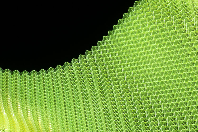 Abstract close-up of a textured green mesh material against a black background, featuring a series of wavy, repetitive patterns.