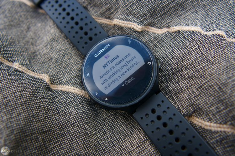 A black Garmin smartwatch displaying a notification from the New York Times about the impact of long working hours on society, resting on a textured fabric surface.