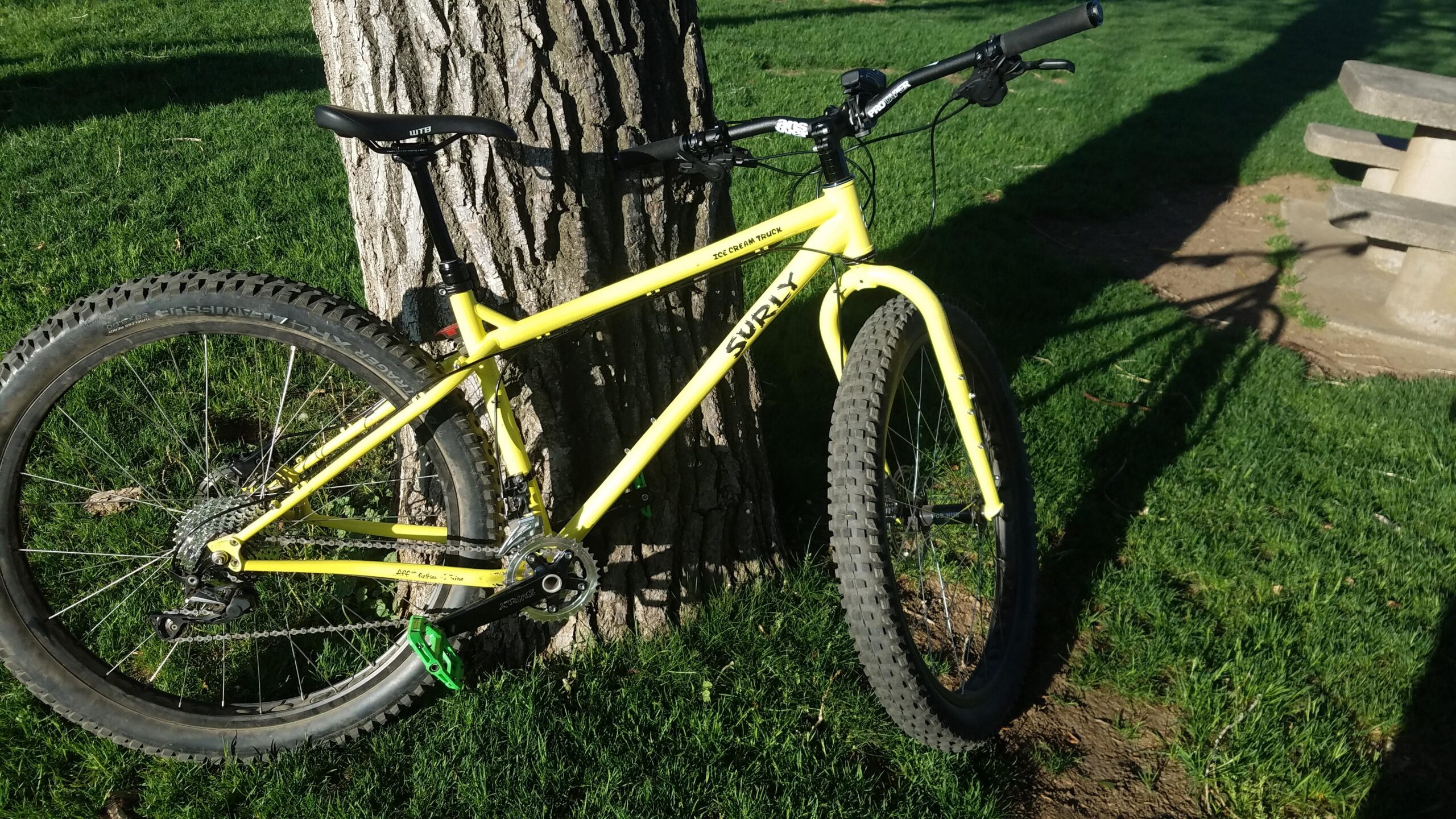 Surly Ice Cream Truck: A bright yellow Surly bicycle leaning against a tree, positioned on green grass, with a picnic table visible in the background.