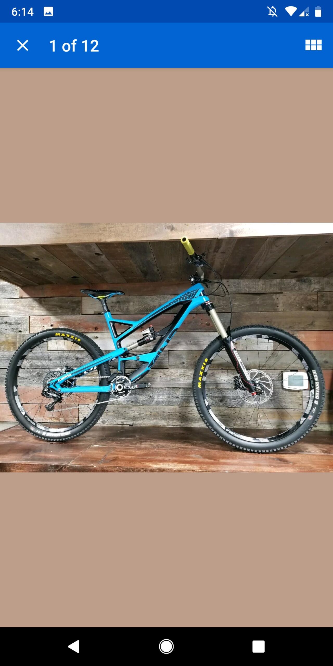 YT Industries CF Pro: A blue mountain bike with a sleek design is displayed against a rustic wooden background. The bike features large, knobby tires labeled "Maxxis," a front suspension fork, and yellow handlebars, showcasing its suitability for off-road cycling.
