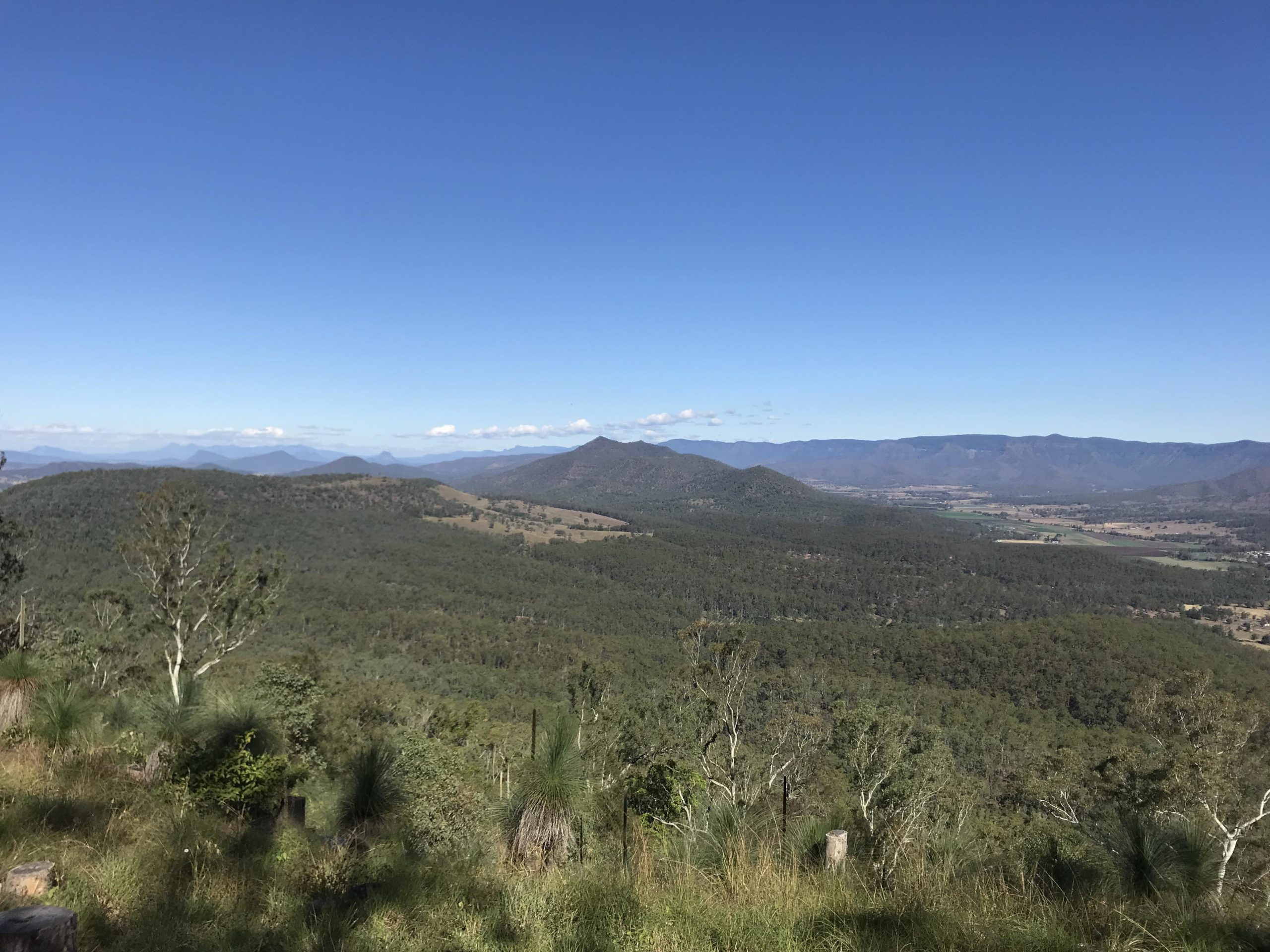 A panoramic view of rolling green hills and distant mountains under a clear blue sky, with patches of vegetation and a sense of tranquility in the landscape. Above 500 mountain bike trail.