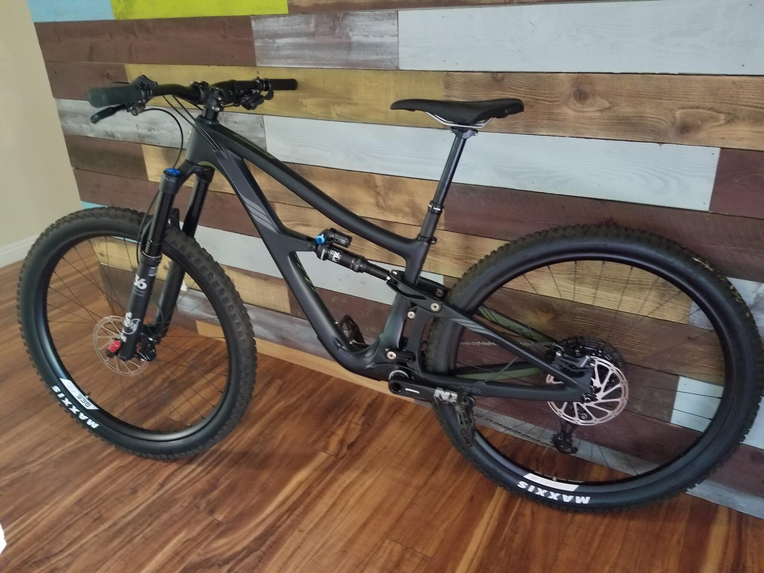 Ibis RipMo: A black mountain bike leaning against a colorful wooden wall, showcasing its sleek frame, thick tires, and front suspension. The floor is wooden, enhancing the warm atmosphere of the setting.