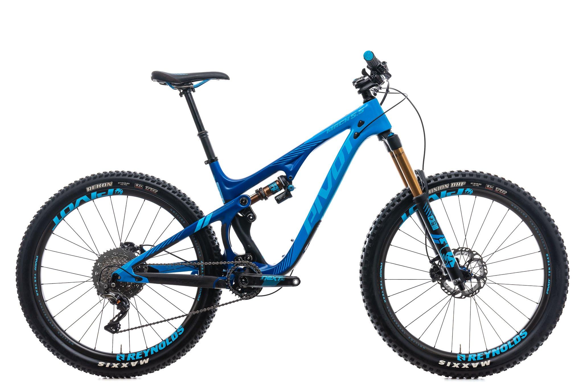 Pivot Mach 5.5: Image of a blue mountain bike with a sleek design, featuring prominent suspension components, wide tires, and a modern frame. The bike is positioned against a white background, emphasizing its details such as the handlebars, saddle, and drivetrain components.